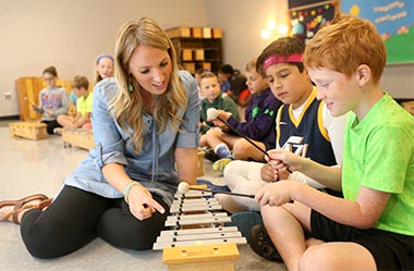 A teacher helping two students learn how to play the xylophone